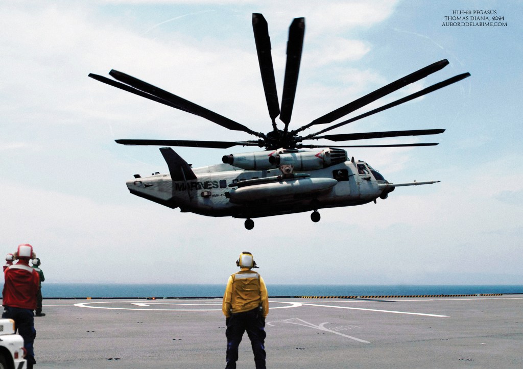 Un hélicoptère militaire fictif de transport lourd avec des rotors contrarotatifs plane au-dessus d'un pont d'envol avec ses rotors en action, tandis que des membres d'équipage en tenue de sécurité observent depuis le pont. L'océan est visible à l'arrière-plan sous un ciel partiellement nuageux.